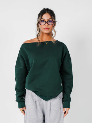 Woman wearing a green off-shoulder sweater and gray pants against a white background