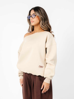 Woman wearing a beige off-shoulder sweater with a logo on a white background