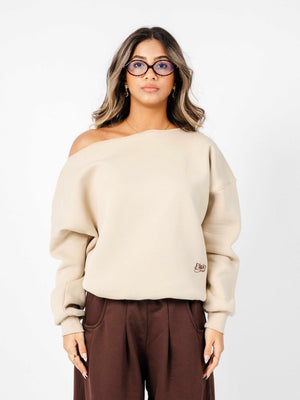 Woman wearing a beige off-shoulder sweater with a logo on a white background