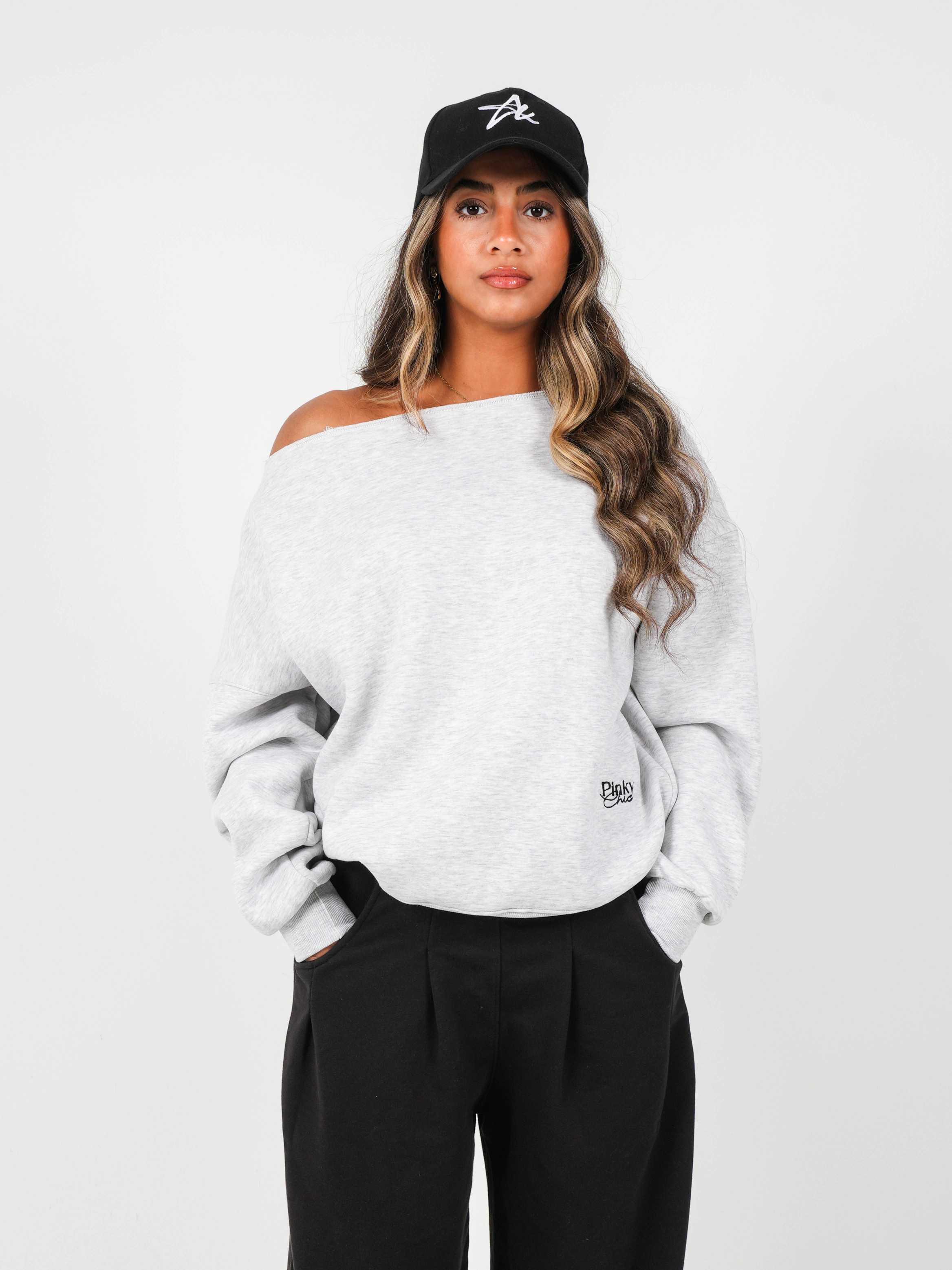 Woman wearing a white off-shoulder sweater and black cap on a plain background