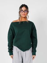 Woman wearing a green off-shoulder sweater and gray pants against a white background