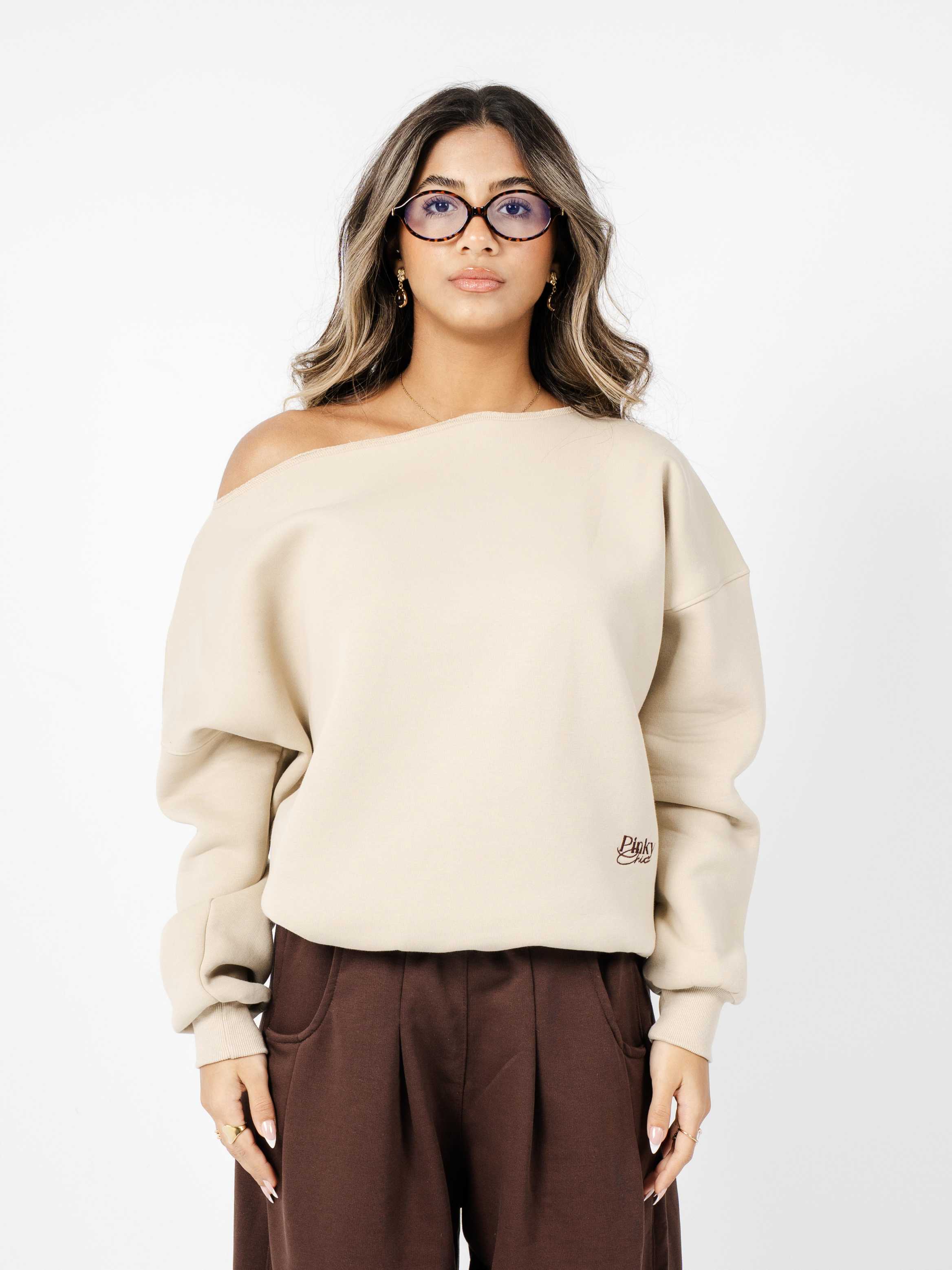 Woman wearing a beige off-shoulder sweater with a logo on a white background